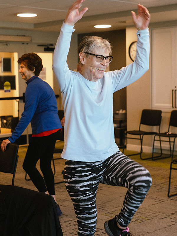 Two seniors exercising with dumbbells in a bright, spacious community room.
