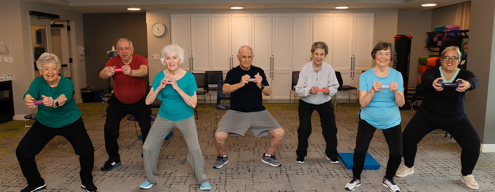 Group exercise session with seniors using small weights in a community room.