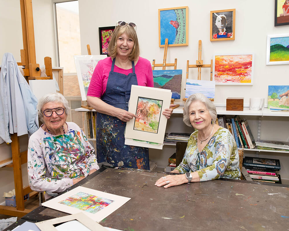 Three women enjoy a painting activity in a colorful art room.