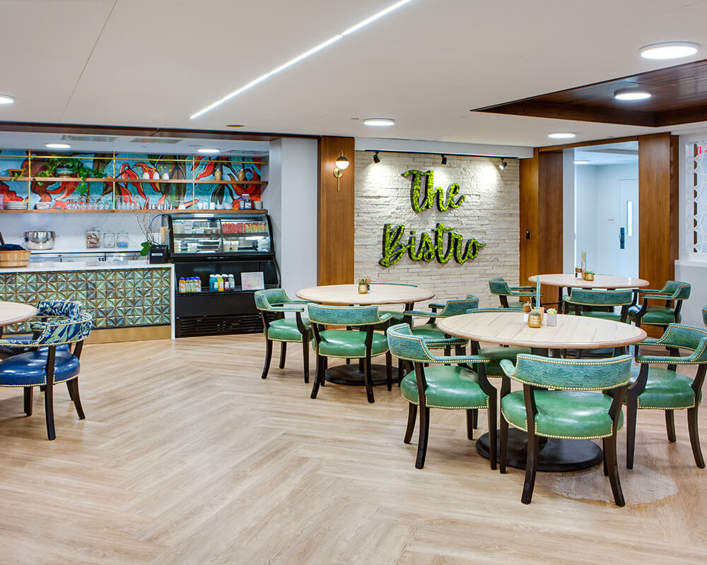 Modern bistro area with green chairs and wooden tables in a cozy senior living community.
