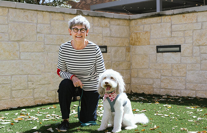 Person with a dog outdoors on artificial grass in a senior living community area.
