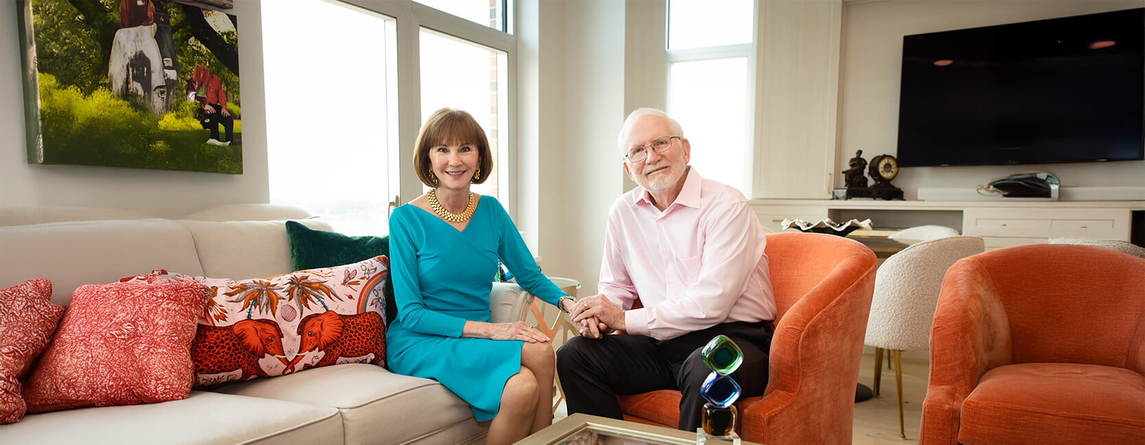 Older couple sitting together in a vibrant, cozy living room with colorful pillows.