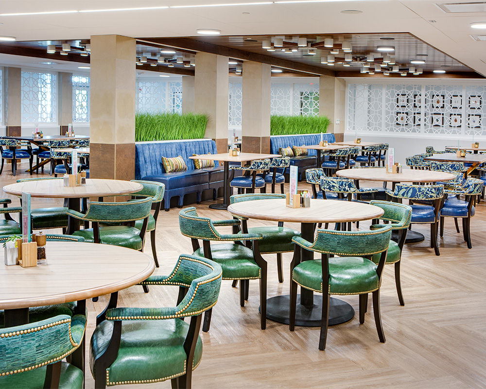 Spacious dining area with green and blue seating at a senior living community.