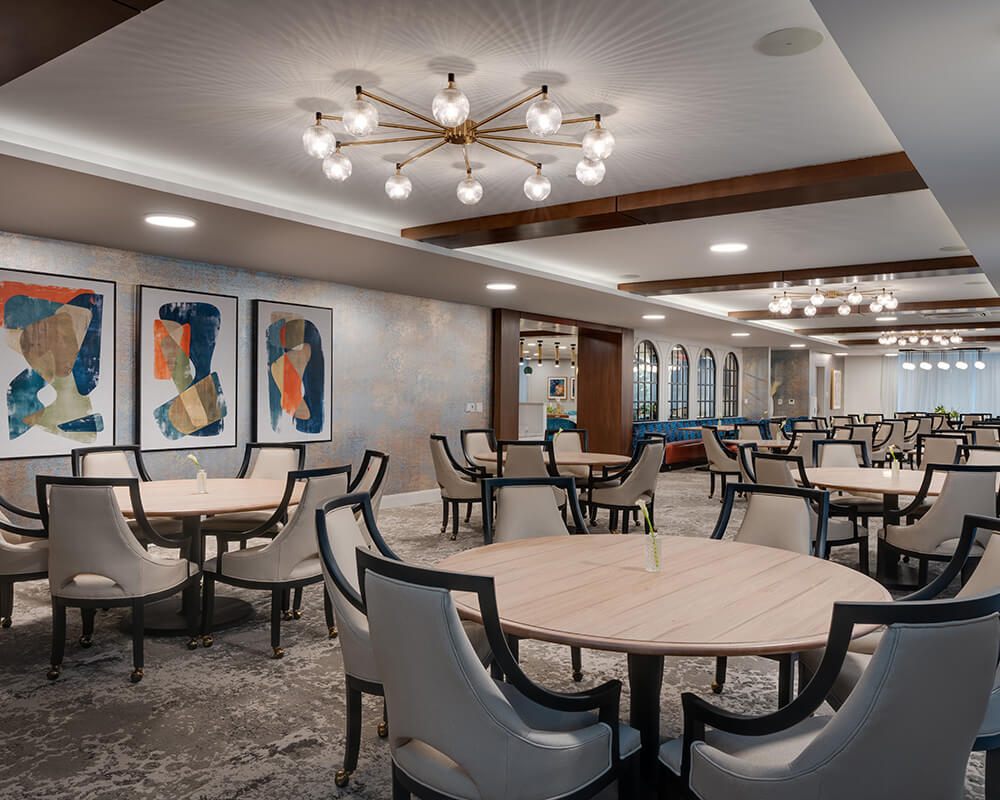 Spacious dining area with round tables and elegant chairs, modern lighting fixtures above.