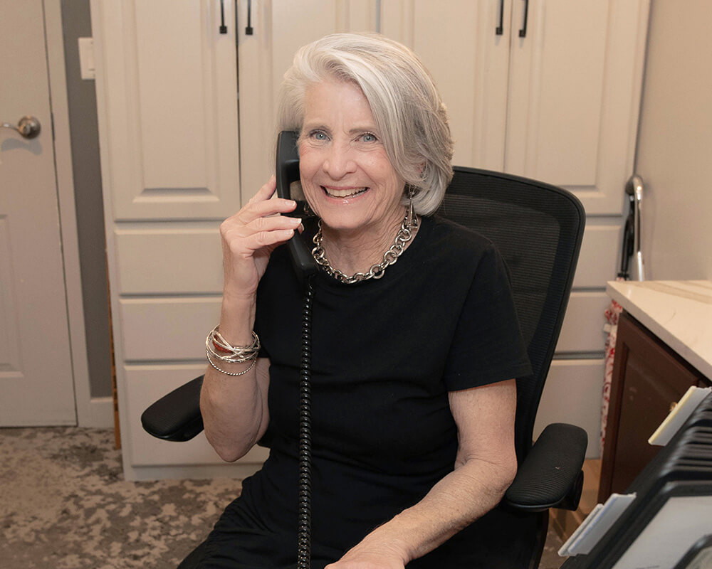 Smiling woman in an office chair talking on a landline phone.