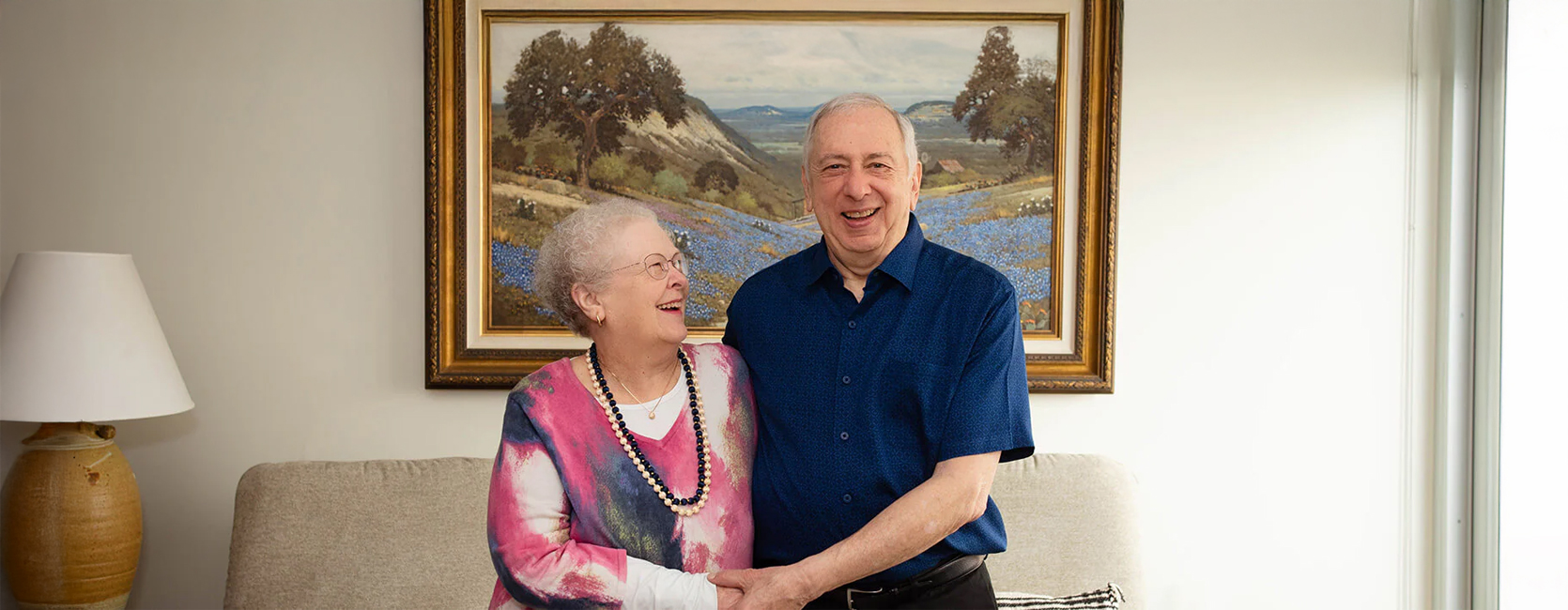 Smiling elderly couple holding hands in a cozy living room setting.