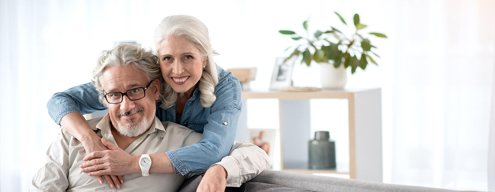 Smiling senior couple embracing on a couch in a bright, modern living space.