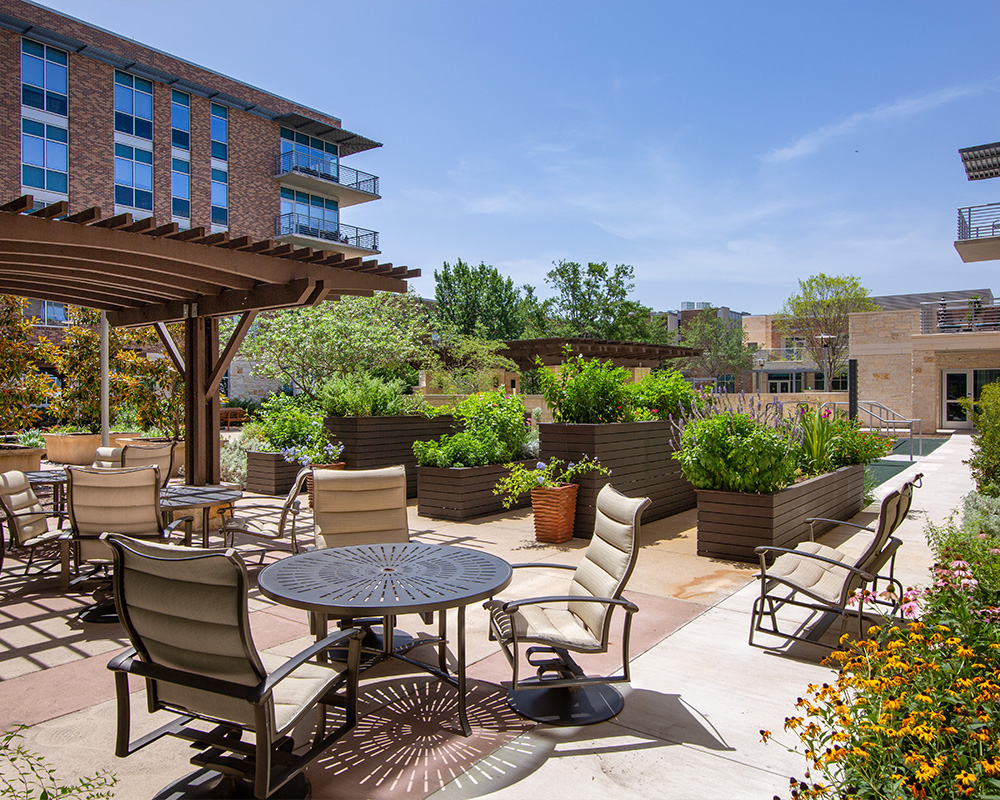 Outdoor lounge area with tables, chairs, and garden in front of a residential building.