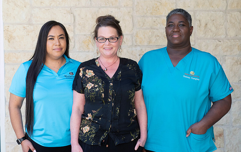 Three rehabilitation staff members smiling in front of a stone wall.
