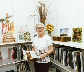 Senior woman in an arts and crafts room surrounded by books and paintings.