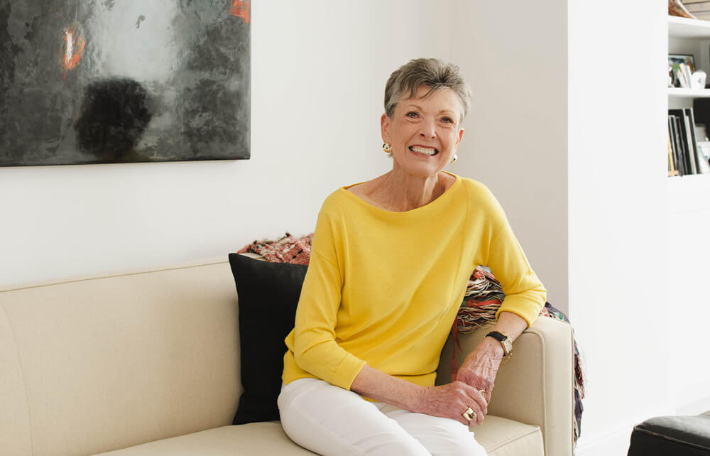 Smiling woman in a yellow sweater sitting on beige sofa in a living unit.