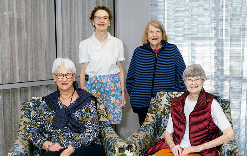 Group of four seniors smiling in a communal area with floral chairs.