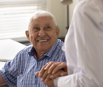 Elderly man in blue shirt smiling at a person in a white coat.