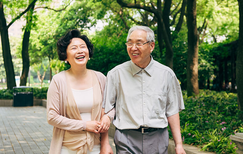 Smiling senior couple walking together in a lush garden path.