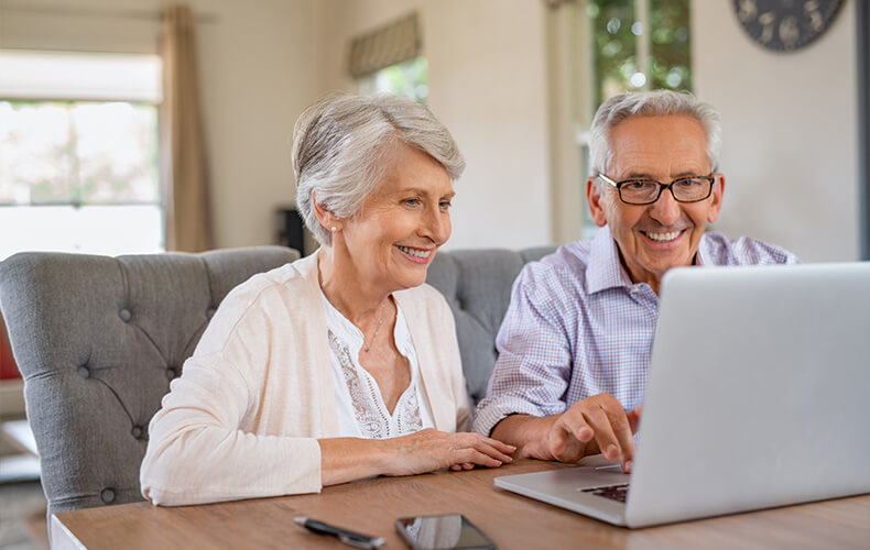 Smiling senior couple using a laptop at home in a bright room.