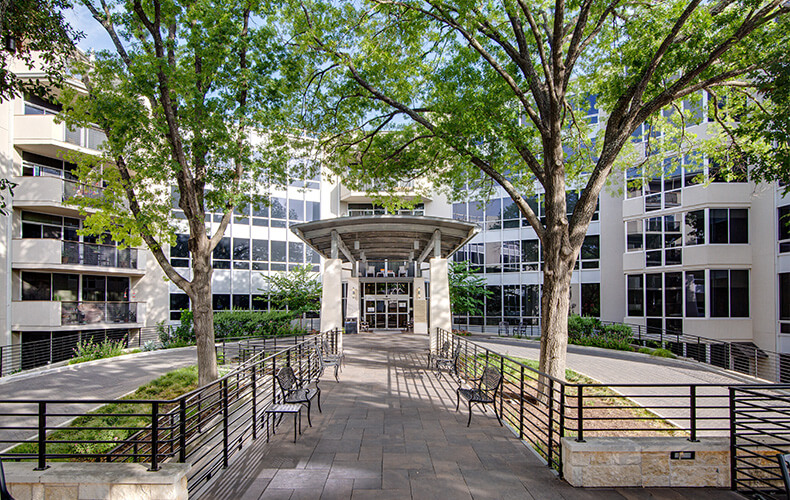 Exterior view of a senior living community building with trees and benches.