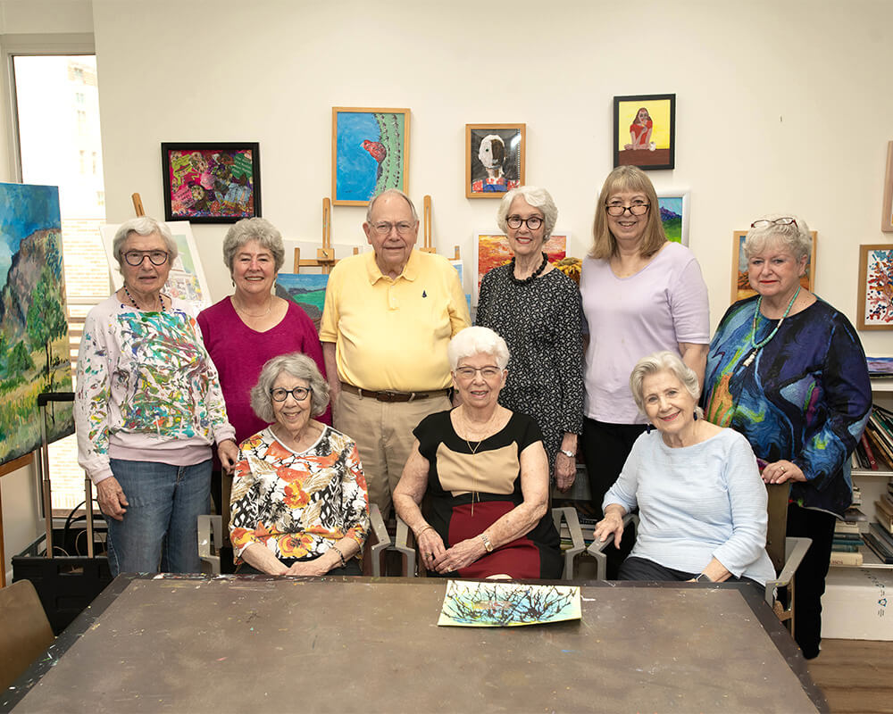 Group of seniors smiling in an art room with colorful paintings on the walls.