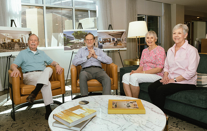 Four seniors sitting together in a common area with architectural plans displayed.