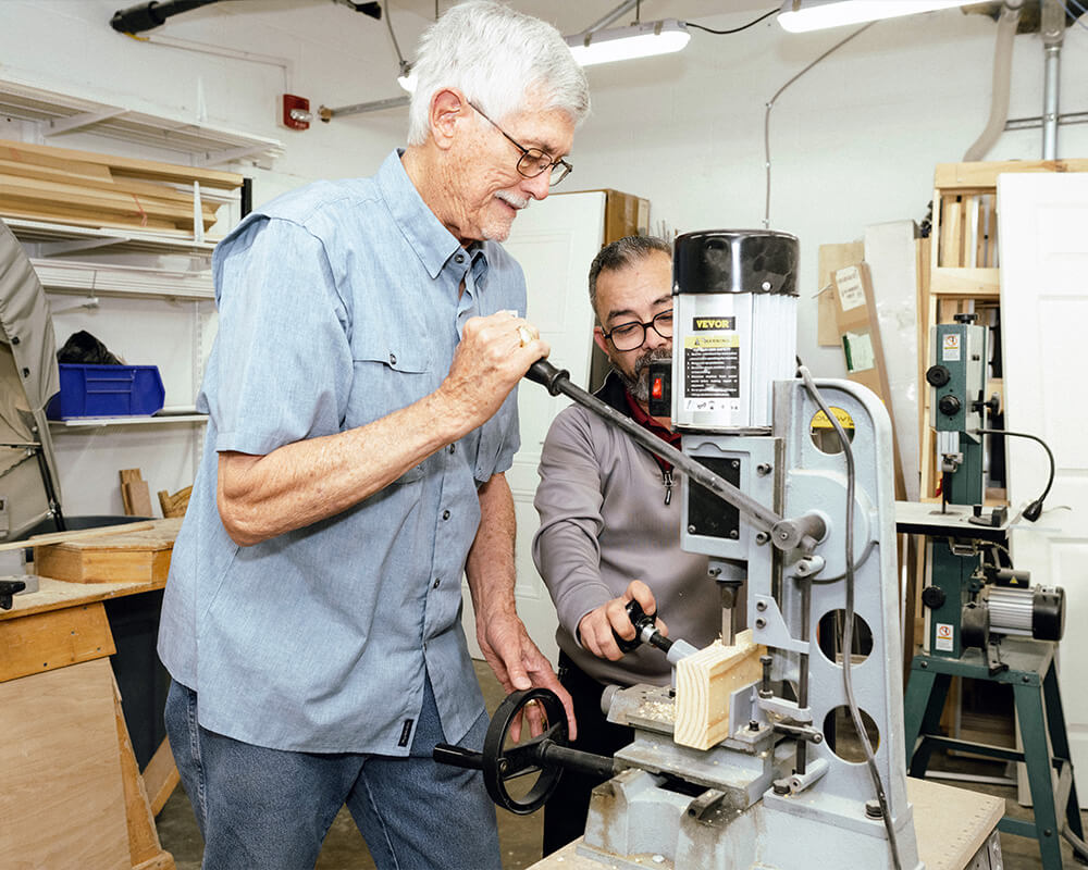 Two senior men working with a wood drilling machine in a workshop.