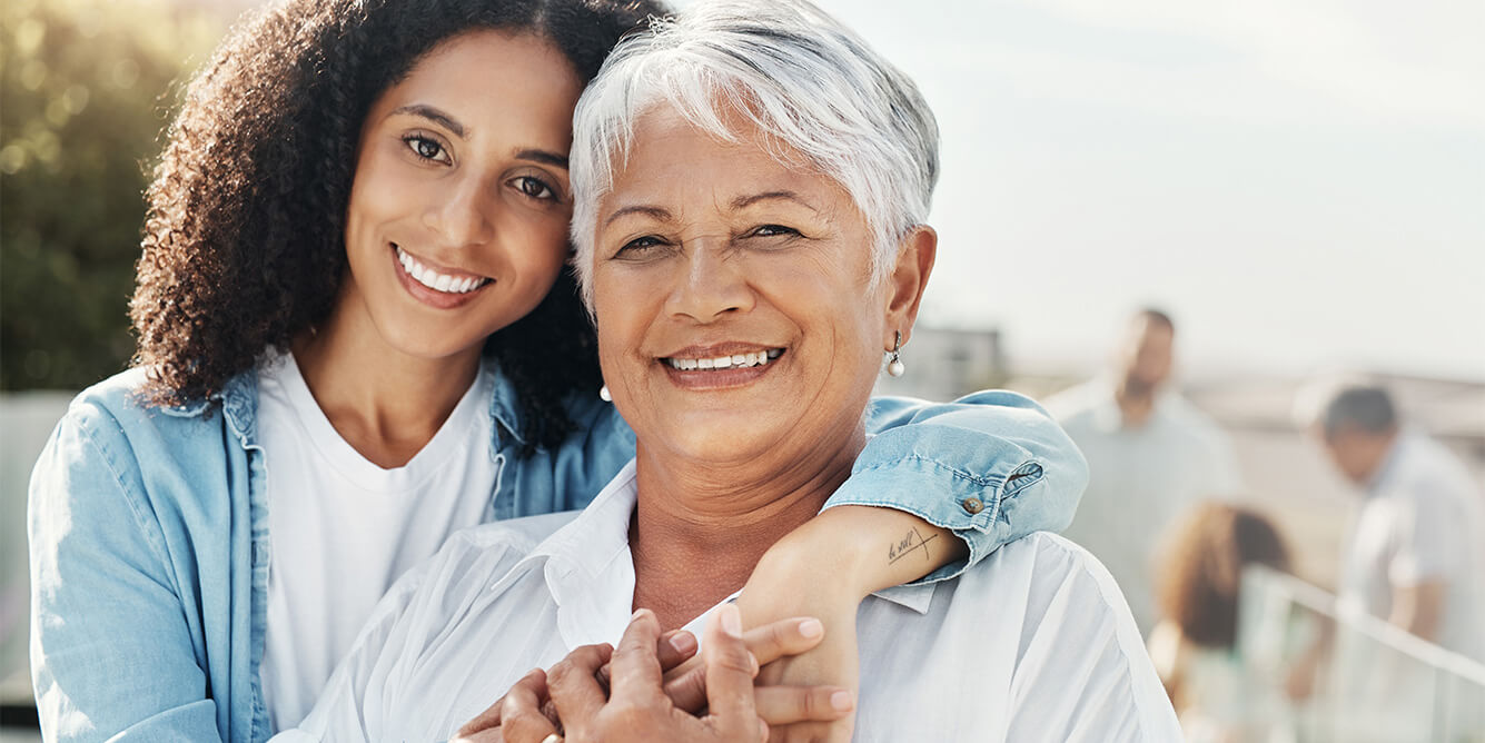 Elderly woman and younger woman smiling outdoors in a community setting.