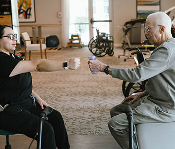 Therapist assisting elder man with arm exercises in a community rehab center.
