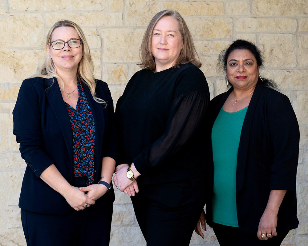 Three team leaders standing in front of a stone wall at a senior living community.
